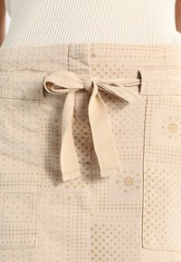 Falda beige con patrón de puntos y estrellas, con un cinturón de tela atado. El material parece ligero y tiene una textura suave.