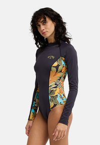 Φόρμα καταδύσεων με μακριά μανίκια σε σκούρο γκρι με πολύχρωμα τροπικά φύλλα στα πλάγια· λεία υφή, εφαρμοστή σχεδίαση και ψηλό γιακά.