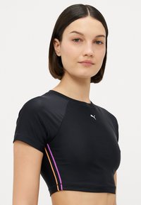 Μαύρο αθλητικό κοντομάνικο μπλουζάκι, με κοντά μανίκια, που διαθέτει ένα μικρό λευκό λογότυπο και πολύχρωμες ρίγες σε μωβ και πορτοκαλί κατά μήκος των πλευρών.