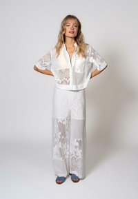 Chemise blanche courte et pantalon large en dentelle avec des motifs floraux et des textures en maille. Présente un devant à boutons et des détails de couture visibles.
