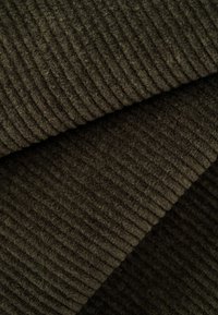 Tessuto in velluto a coste verde scuro con texture a righe verticali e superficie morbida e pelosa, che mostra strati sovrapposti per un effetto di profondità.