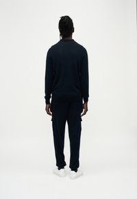 Σκούρα ναυτικό μπλούζα  και αντίστοιχο παντελόνι cargo, κατασκευασμένα από μαλακό υλικό. Διαθέτουν εφαρμογή slim, δύο τσέπες cargo και λευκά αθλητικά παπούτσια.