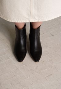 Svarta läderankelstövlar med spetsig tå och en åtsittande passform. Texturen är slät och klacken saknas, vilket ger en minimalistisk design.