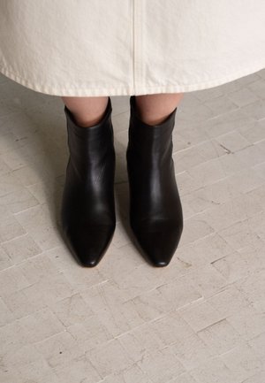 Stivaletti alla caviglia in pelle nera con punta appuntita e vestibilità aderente. La texture è liscia e il tacco è assente, offrendo un design minimalista.