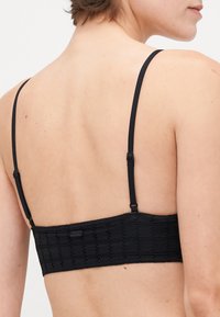 Zwarte kanten bralette met verstelbare dunne bandjes, een textuurpatroon met geometrische openingen en een rechthoekig rugontwerp.