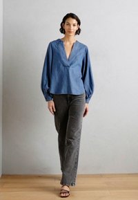 Lys blå denimbluse med v-hals og vide ærmer, parret med grå lige bukser og sorte stroppestøvler.