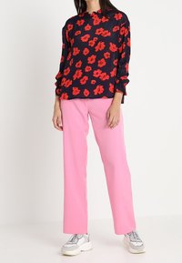 Top blu navy con motivo floreale rosso, maniche lunghe con polsini arricciati; abbinato a pantaloni dritti rosa chiaro e sneakers grigie.