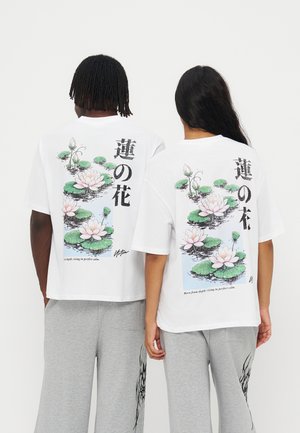 Dvaja ľudia nosiaci biele tričká s dizajnom lotosového kvetu a plávajúcich listov a vertikálny japonský text na chrbte.