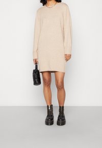 Vestido de punto beige con mangas largas y puños acanalados, combinado con botas de plataforma negras y un pequeño bolso negro.