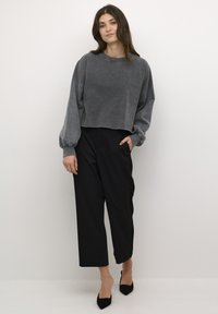 Pilkas trumpas megztinis su nuleistomis pečių siūlėmis, suplėšyta apatine dalimi ir juodomis aukšto liemens kelnėmis; derinamas su juodomis smailiomis aukštakulnėmis bateliais.