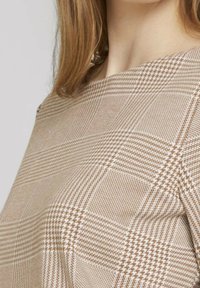 Top de cuadros marrón y beige con una textura suave, que presenta patrones a rayas y un escote redondeado, exhibido en un ángulo.