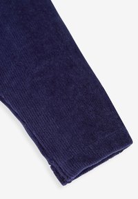 Marineblauwe, zachte corduroy stof, met een verticale ribbelstructuur en een omgevouwen rand bij de manchetten. Rijke kleur met een gladde afwerking.