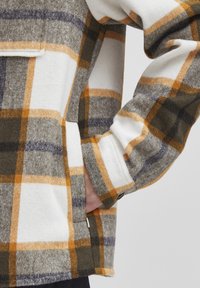 Button-up flannel shirt in plaid pattern. Features gray, white, orange, and navy colors. Soft texture with a relaxed fit. Includes side pocket.