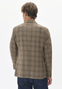 Brązowy blazer w kratę, wykonany z teksturowanej tkaniny, z wysmuklonym kołnierzykiem i złotymi guzikami na mankietach. Widoczny detal z tylnym rozporkiem.