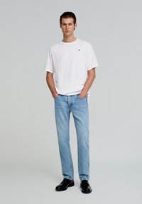 Witte korte mouwen T-shirt met een klein logo, gecombineerd met lichtblauwe rechtgesneden jeans en zwarte veterschoenen. Eenvoudig ontwerp en kleurenschema.