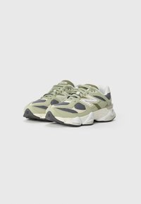 Lys grønn og grå sneakers med mesh- og semsket skinnmaterialer, rund form, polstret tunge og tykk såle. Har stort logo detaljer på siden.