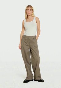 Top bianco senza maniche abbinato a pantaloni khaki a vita alta e larghi. I pantaloni hanno cerniere laterali e una consistenza liscia. Scarpe nere.