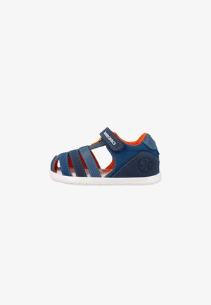 Sandalia de niño azul marino y naranja con puntera cerrada, correa de Velcro y suela blanca, diseñada para comodidad y soporte.