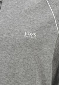 Felpa grigia con zip realizzata in tessuto morbido, con dettagli in piping bianco e un logo ricamato "BOSS HUGO BOSS" sul petto.