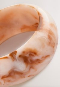 Translucent bangle made of smooth, glossy resin featuring a marbled pattern in soft peach and brown tones, with a rounded shape.