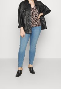 Chemise-veste oversized en cuir noir, top à imprimé léopard rose, jeans skinny bleu clair et mules noires à talons. Un style simple et moderne.
