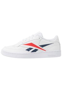 Vita Reebok låga sneakers med röda och marinblå snedställda ränder och en texturerad vit sula mot en enkel bakgrund.