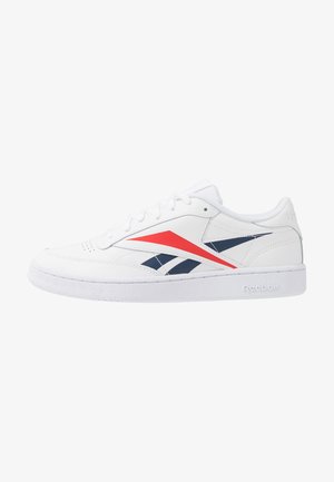 Sneaker Reebok bianco a collo basso con strisce angolari rosse e blu navy e suola bianca testurizzata su uno sfondo neutro.