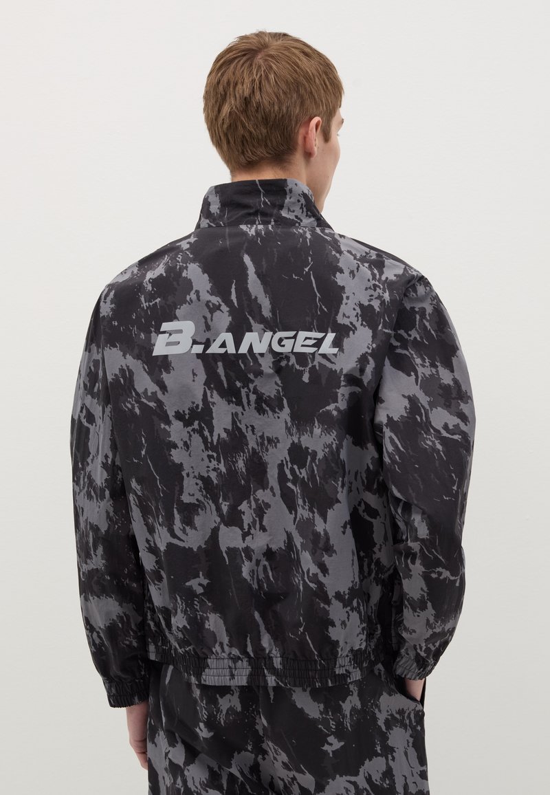 Giacca marmorizzata nera e grigia con colletto alto, polsini elastici e un logo sul retro. Realizzata in un materiale leggero e liscio.