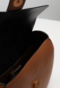 Braune strukturierte Ledertasche mit schwarzem Innenraum, ausgestattet mit einem goldenen Knopfverschluss und einer eleganten, runden Form.