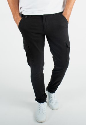 Pantalons cargo noirs avec poches latérales, design cintré et texture lisse; associés à des baskets blanches.