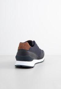 Marinblå sneakers med överdel i läder och textil, bruna mockadetaljer, vit mellansula och gummisula. Har strukturerad yta och perforeringar.