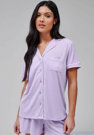 Ensemble de pyjama lavande à manches courtes comprenant un haut boutonné avec une poche et un passepoil blanc ; tissu doux et texturé, shorts à coupe décontractée.