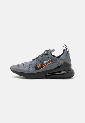 Chaussure de sport grise et noire avec logos Nike swoosh orange et noir et une semelle à coussin d’air visible sur fond blanc.
