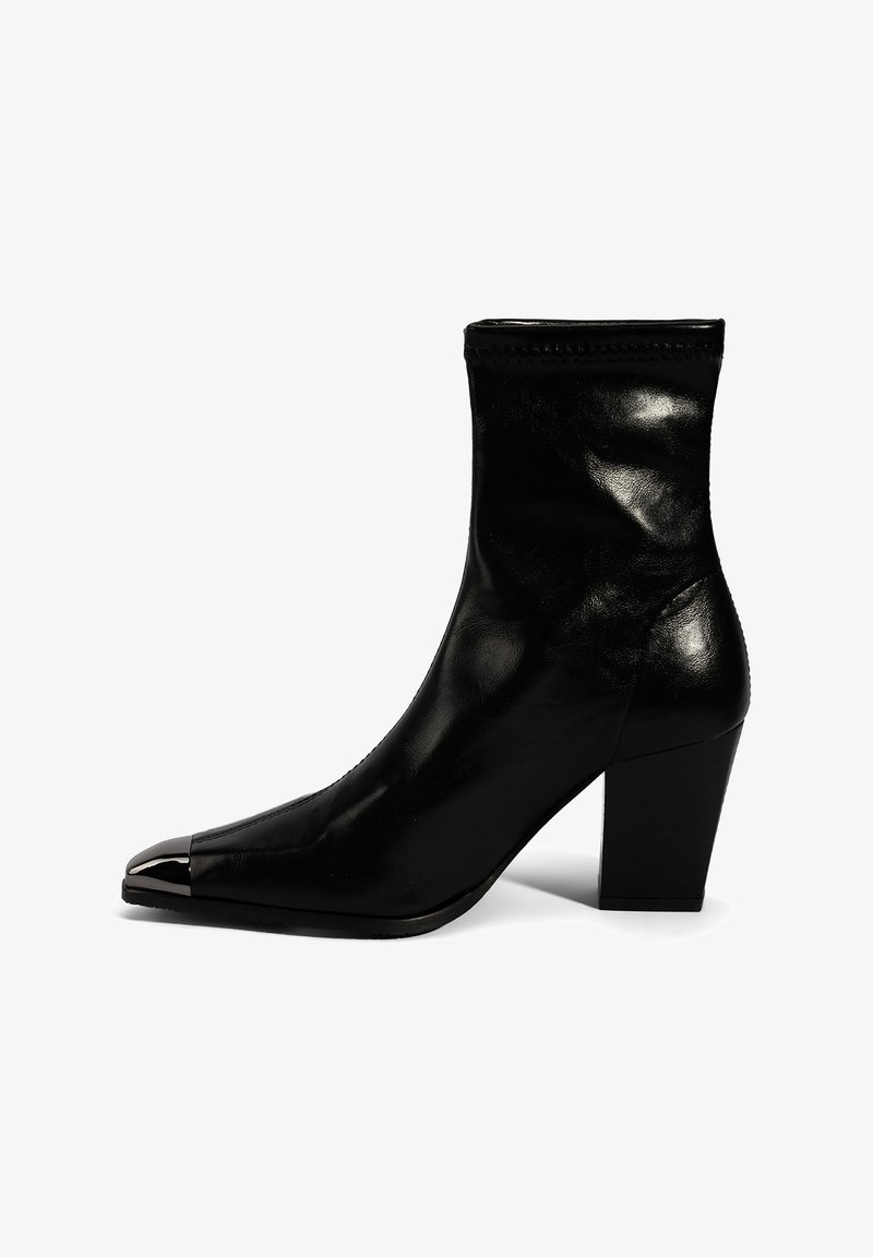 Bottine en cuir noir à bout pointu, avec un accent métallique sur le capuchon, et un talon empilé. Texture lisse et design épuré.