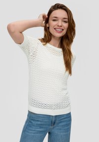 Biały sweter dzianinowy z falistym wzorem, krótki rękaw i okrągły dekolt; zestawiony z niebieskimi dżinsami. Gładka tekstura, lekka konstrukcja.