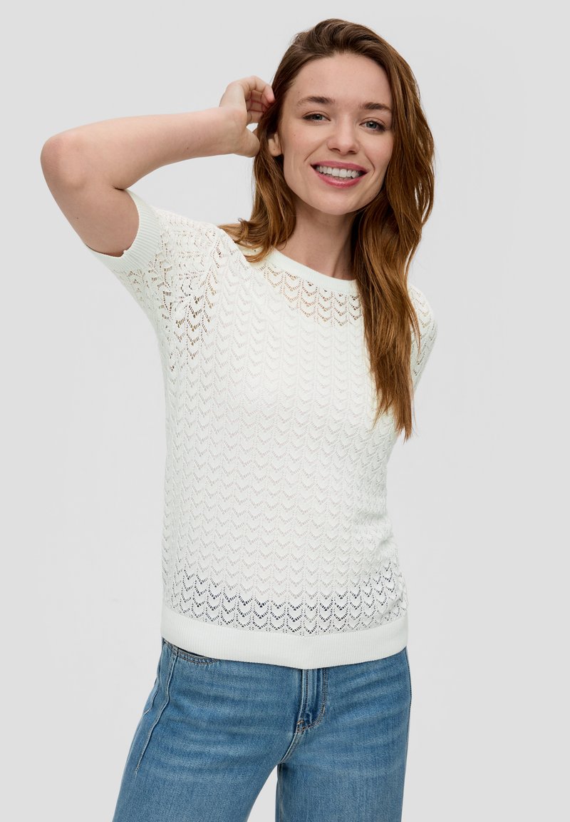 Biały sweter dzianinowy z falistym wzorem, krótki rękaw i okrągły dekolt; zestawiony z niebieskimi dżinsami. Gładka tekstura, lekka konstrukcja.