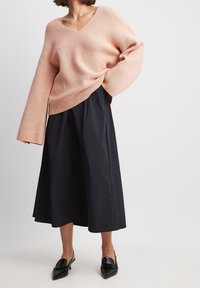 Vaaleanpunainen ribbiknitti villapaita V-pääntiellä, yhdistetty mustaan laskostettuun midi-hameeseen. Mustat loaferit viimeistelevät asun.
