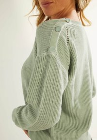 Light green knit sweater with a textured pattern and functional silver buttons on the shoulder. Soft, casual design with ribbed cuffs.
