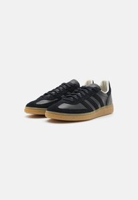 Black suede and leather sneakers with gum rubber sole. Features textured upper, three dark stripes, and round laces. Low-profile design.