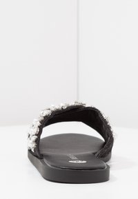 Svart slip-in sandal med en platt design, smyckad med klara och pärlliknande pärlor längs remmen. Slät sula, minimalistisk stil.