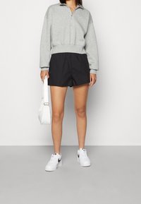 Šedá mikina na zip, černé kraťasy, bílé tenisky s černými detaily a bílá kabelka. Jednoduchý design a pohodlný střih.