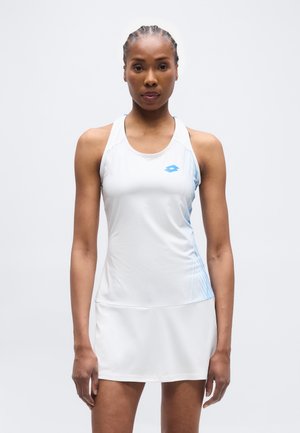 Atletische vrouw met gevlochten haar, gekleed in een mouwloze witte sportjurk met lichtblauwe accenten, staand tegen een effen achtergrond.