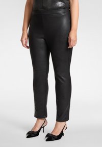 Zwarte nepleren broek met een slanke pasvorm en een gladde textuur, voorzien van een hoge tailleband en minimale stikseldetails.