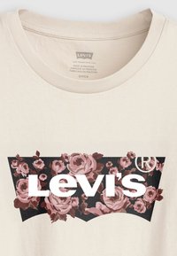 Krämfärgad bomulls T-shirt med en svart och blommig design, prydd med rosa rosor och en framträdande vit "Levi's"-logotyp i mitten.