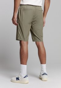 Olijfgroene shorts met elastische tailleband, twee achterzakken en een relaxte pasvorm, gecombineerd met witte sneakers en korte sokken.