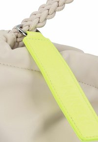 Sac en cuir beige avec une poignée tressée, arborant une étiquette jaune vif avec du texte en relief. Texture lisse et design minimaliste.