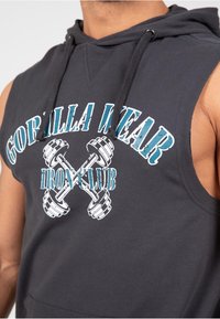 Zwarte mouwloze hoodie met op de voorkant de grafische tekst "GORILLA WEAR" en gekruiste dumbbells. Zacht katoenen materiaal met een relaxte pasvorm en capuchon.