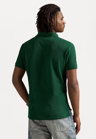Polo de color verde oscuro, de manga corta, con tejido texturizado y dobladillo recto. Presenta una apertura en cada lado cerca de la parte inferior.