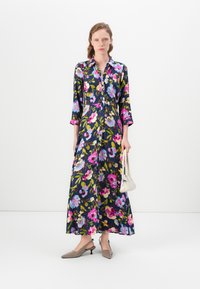 Floral, navy long dress with a button-down front, three-quarter sleeves, and vibrant pink, blue, and green patterns. Model holds a small white bag.