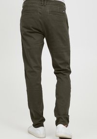 Dark green cotton chinos with a slim fit, featuring back pockets and a zipper fly, paired with white sneakers.
